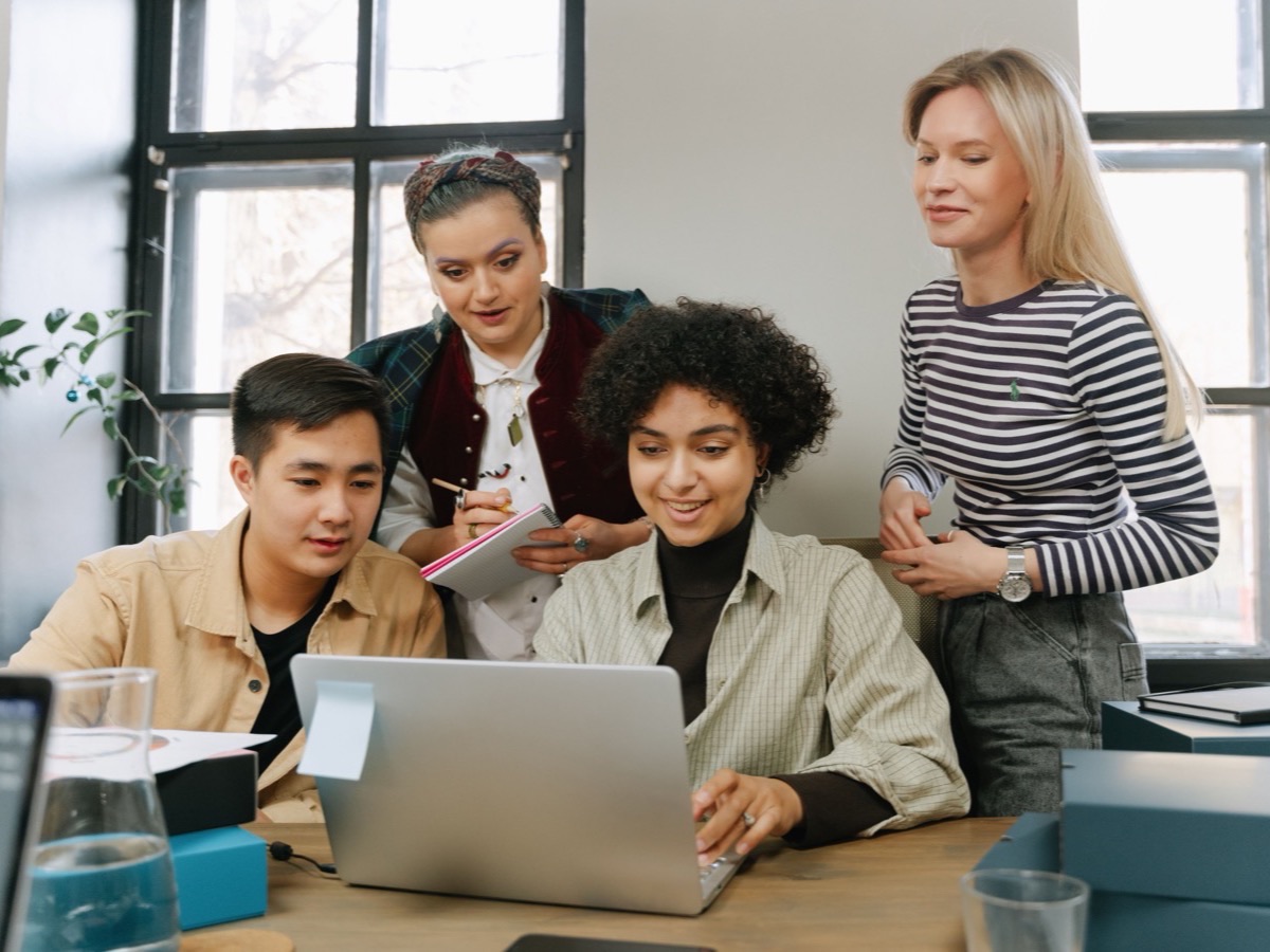 Four colleagues gathered around a laptop in a bright office