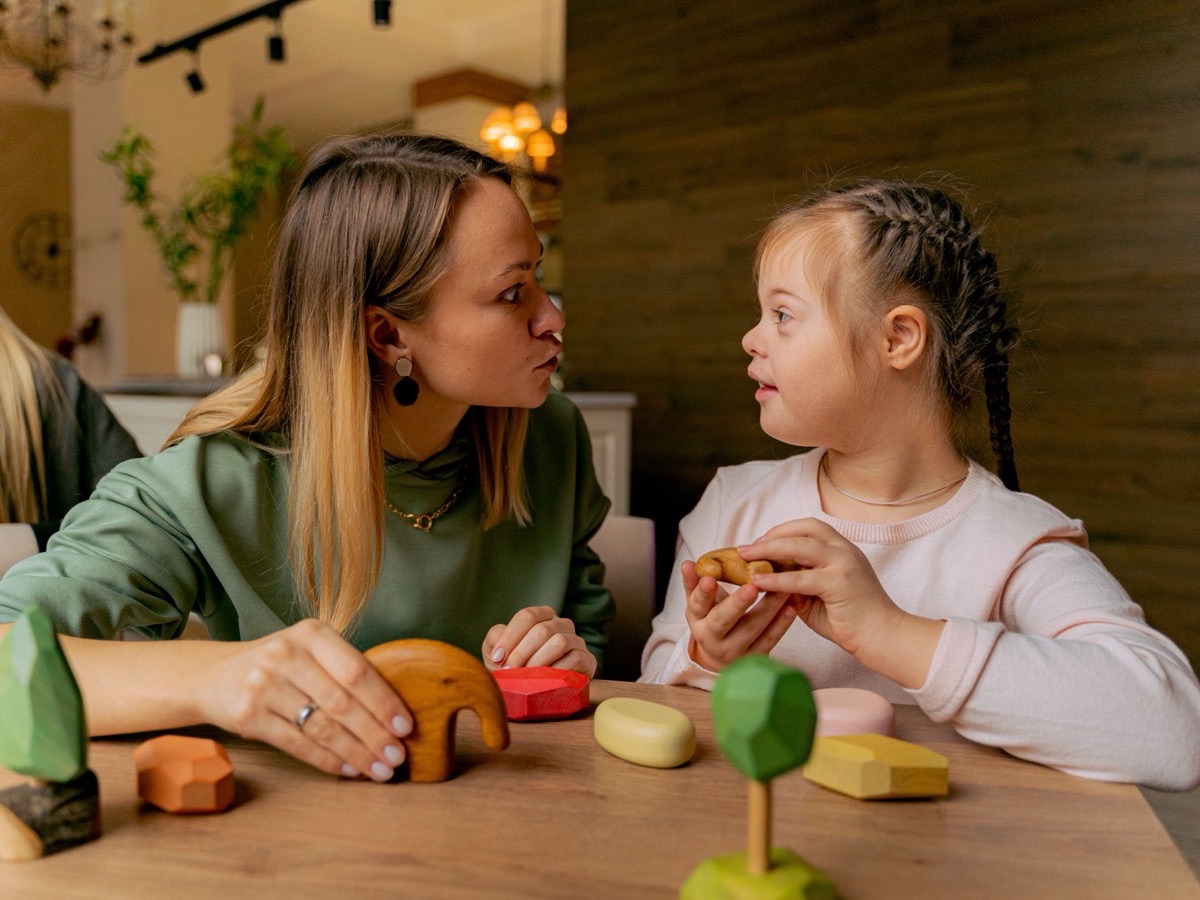 A therapist and a young girl talking across a table of wooden toys