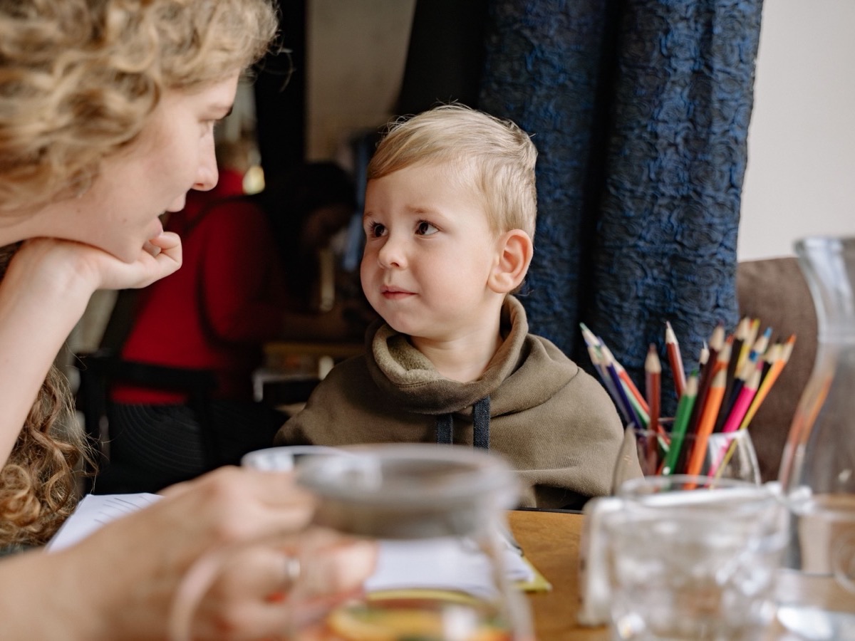 A woman leaning in to talk with a small child at a table