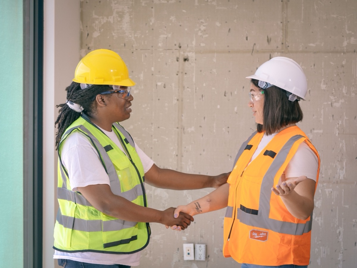 Two workers in hi-vis and hard hats talking on a construction site